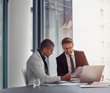 Two businessmen discussing work at office desk.